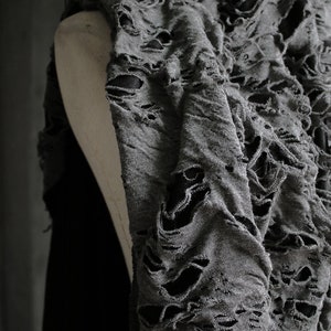 May include: Gray distressed fabric with large holes throughout. The fabric is draped over a mannequin.