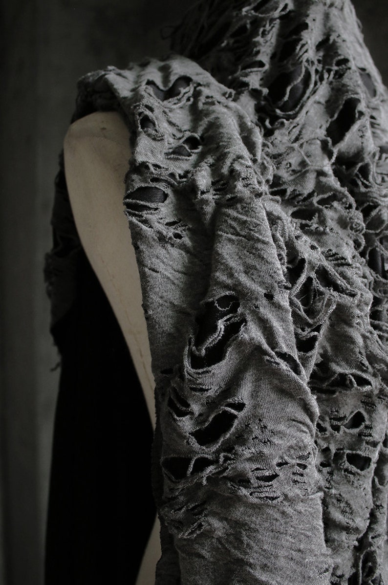 May include: Gray distressed fabric with large holes throughout. The fabric is draped over a mannequin.
