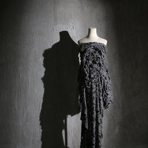 May include: A gray dress with a ruffled texture on a white mannequin against a gray concrete wall.