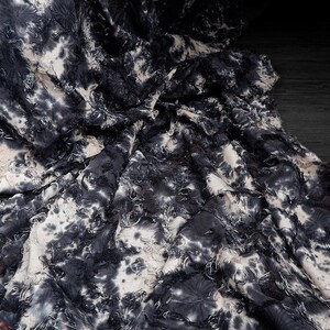 May include: Close-up of a fabric with a tie-dye pattern in shades of black, white, and gray. The fabric has a textured, frayed appearance, with visible threads and a crinkled texture. The overall effect is a dark, artistic textile.