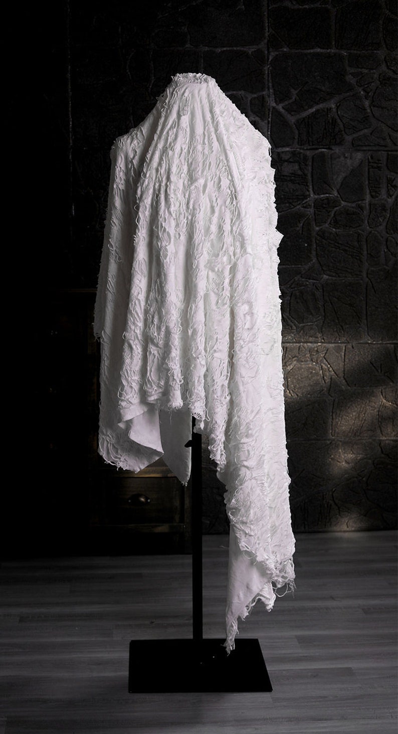 May include: White fabric with a textured, crinkled surface draped over a black stand. The fabric has a frayed edge and is displayed against a dark background.