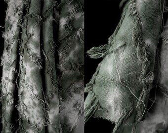 May include: Close-up of a gray and white tie-dye fabric with frayed edges. The fabric is soft and textured, with a subtle sheen.