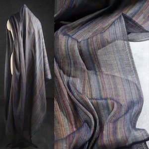 Op de afbeelding: Een gedrapeerde stof met verticale strepen in tinten blauw, paars, bruin en goud. De stof wordt getoond op een mannequin, met een close-up die de textuur en kleurvariaties laat zien. Het materiaal lijkt licht en vloeiend.