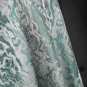 K&ouml;nnte beinhalten: Nahaufnahme eines teal- und wei&szlig;en Stoffes mit Marmormuster. Der Stoff hat eine strukturierte, gewebte Optik.