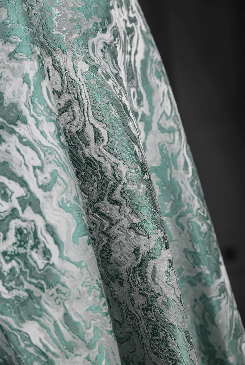 K&ouml;nnte beinhalten: Nahaufnahme eines teal- und wei&szlig;en Stoffes mit Marmormuster. Der Stoff hat eine strukturierte, gewebte Optik.