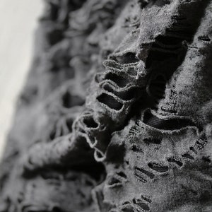 May include: Close-up of a gray fabric with distressed holes and frayed edges.