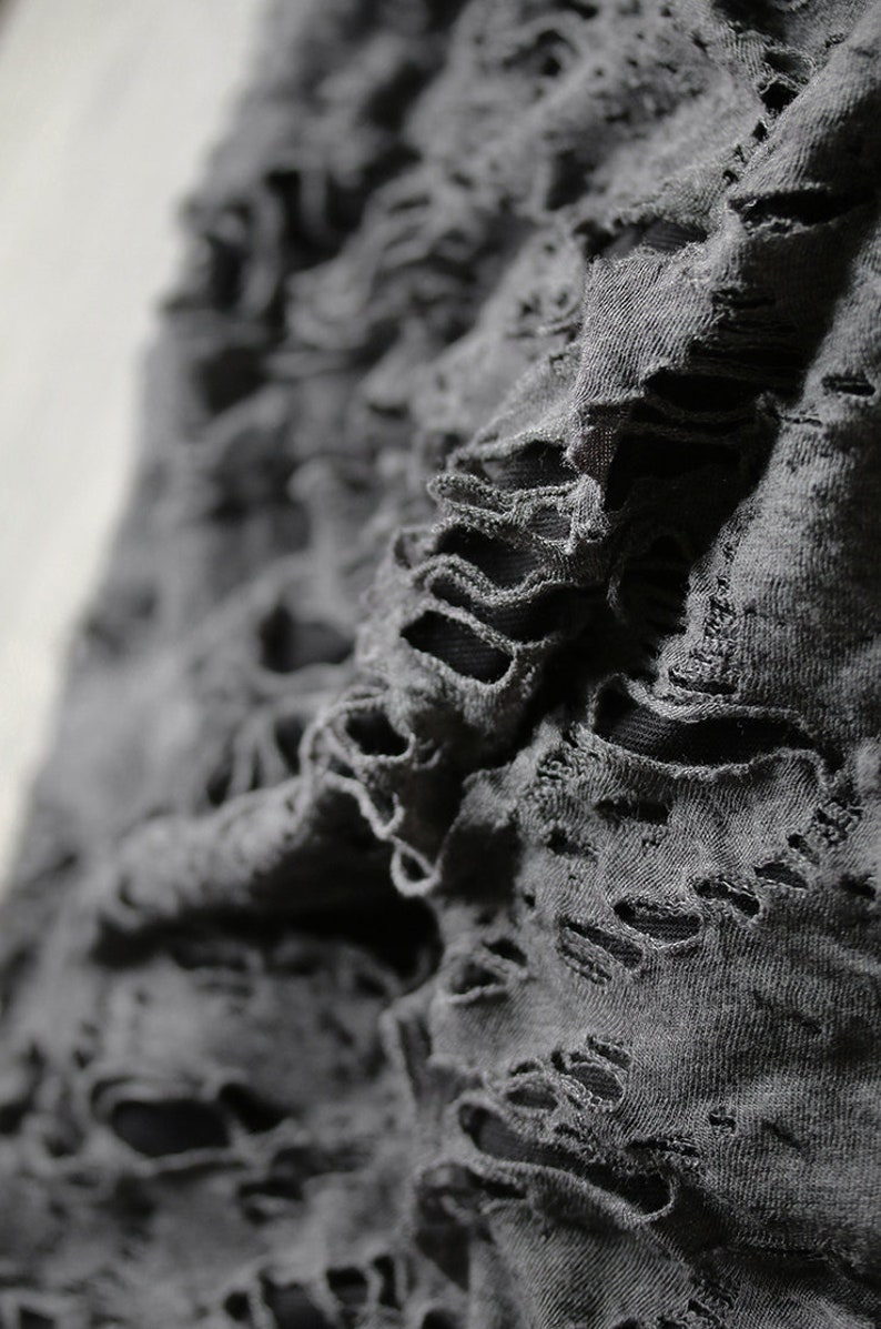 May include: Close-up of a gray fabric with distressed holes and frayed edges.