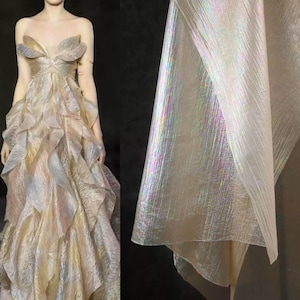 Puede incluir: Un vestido largo sin tirantes con una falda con volantes en capas. El vestido presenta una tela brillante e iridiscente en tonos dorados, rosas y azules. El corpiño tiene un diseño en forma de pétalo. Una muestra de la tela se muestra a la derecha.