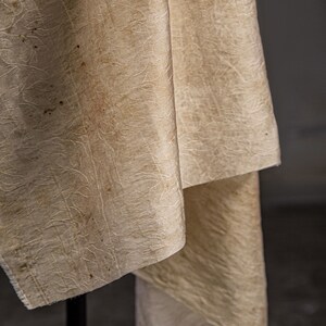May include: A close-up of a cream-colored fabric with a textured pattern. The fabric is folded and draped over a black surface.