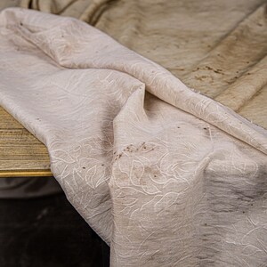 May include: A white tablecloth with a subtle floral pattern and brown stains. The tablecloth is folded and draped over a wooden surface.