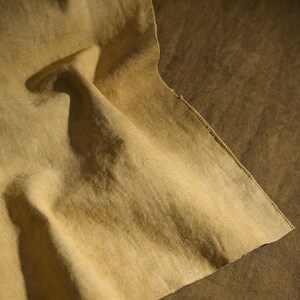 K&ouml;nnte beinhalten: Nahaufnahme eines St&uuml;cks beigen Stoffes mit rauer Textur. Der Stoff ist gefaltet, wodurch Schatten entstehen und die Textur hervorgehoben wird. Die Kanten des Stoffes sind sichtbar und zeigen eine Naht. Die Gesamtpalette ist erdig, mit Variationen von Beige und Braun.