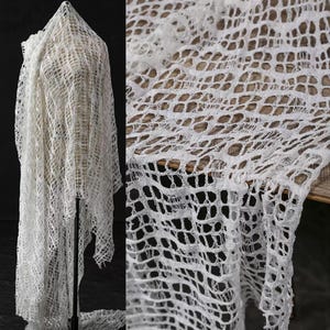 May include: White crochet fabric with a delicate, open-weave pattern. The fabric is draped over a mannequin and appears to be lightweight and airy.