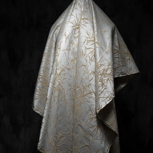 May include: A white fabric with a gold bamboo pattern draped over a dark background.