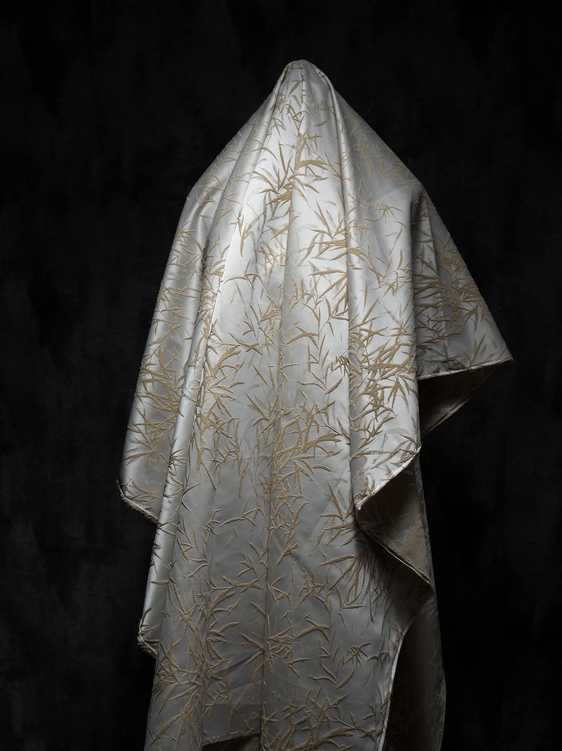May include: A white fabric with a gold bamboo pattern draped over a dark background.