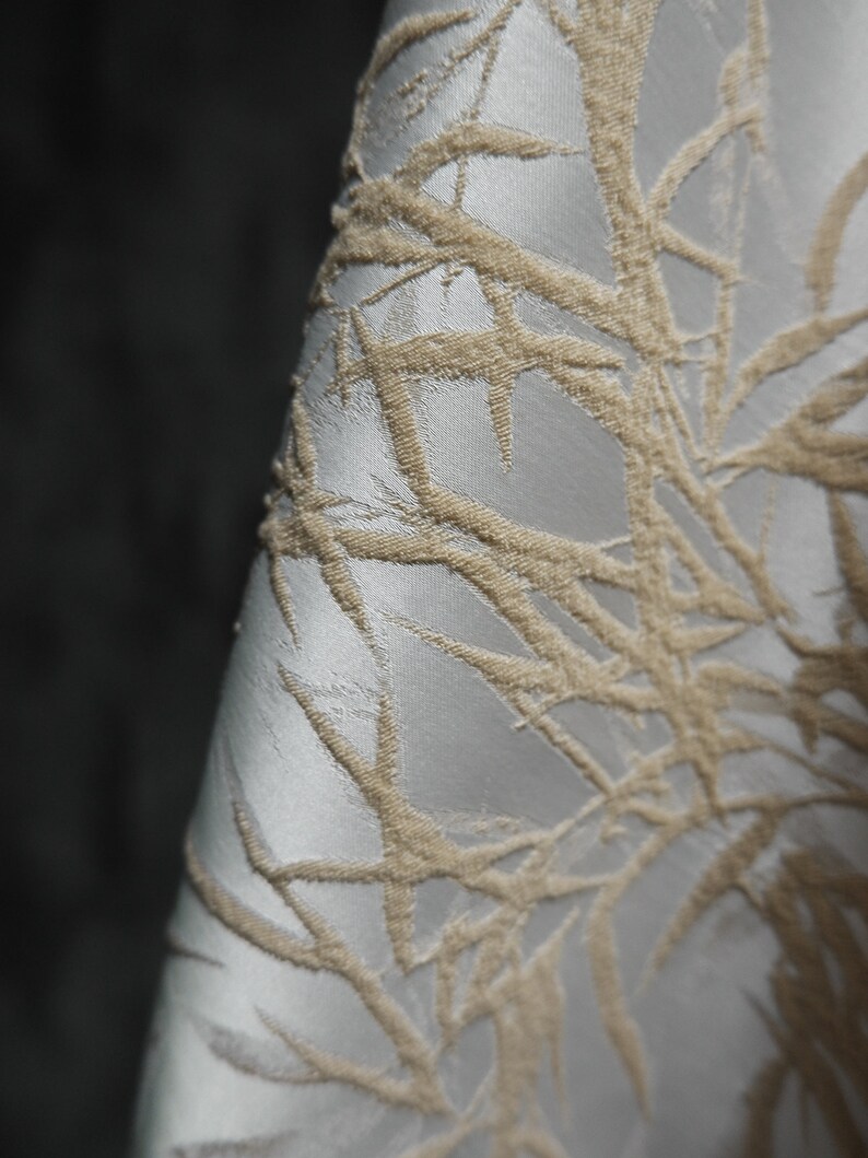 May include: Close-up of a white fabric with a raised, beige, geometric pattern. The pattern resembles branches or leaves.