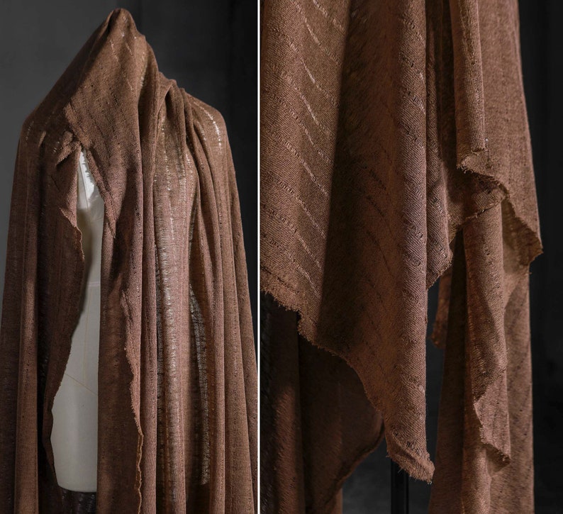 May include: A brown linen fabric with a subtle striped pattern. The fabric is draped over a mannequin and folded on a table.