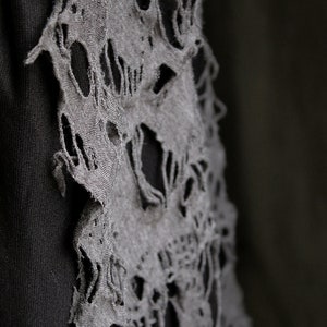 May include: A black fabric garment with a gray fabric overlay. The overlay has a distressed, ripped design that resembles a skull.