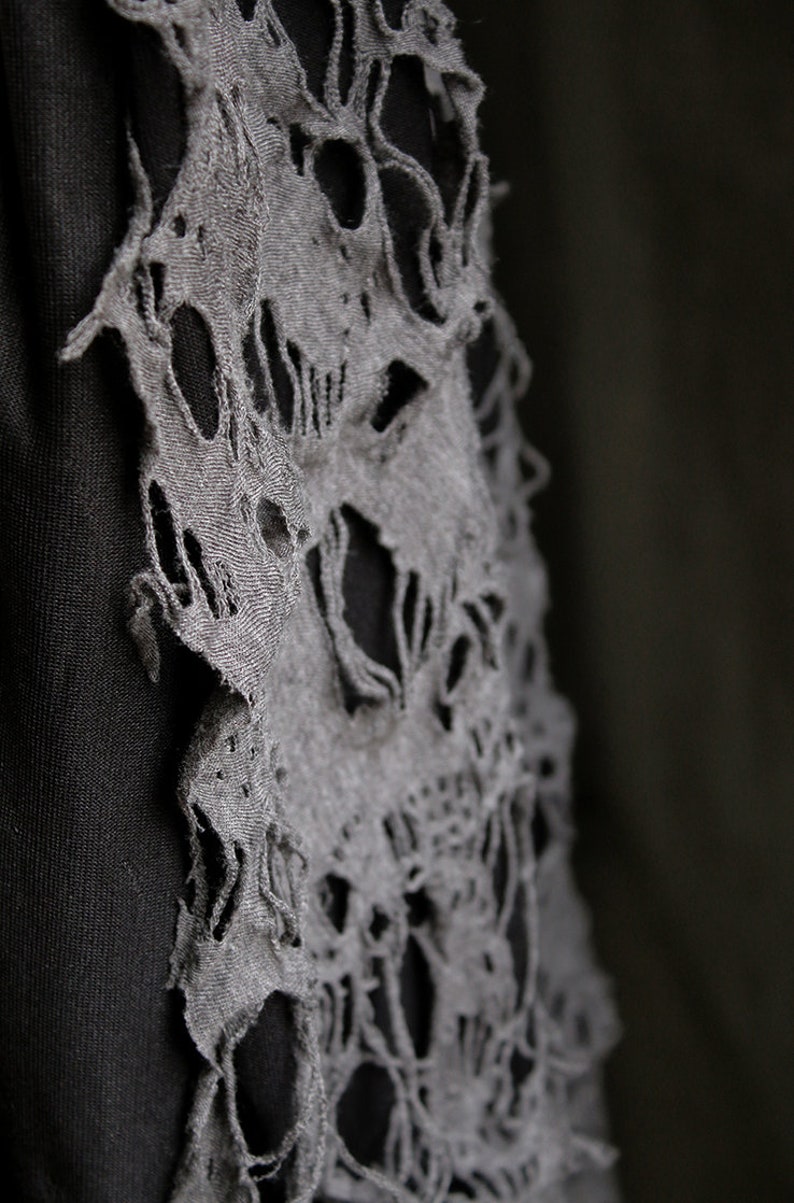 May include: A black fabric garment with a gray fabric overlay. The overlay has a distressed, ripped design that resembles a skull.