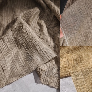 Peut inclure: Gros plan sur un tissu texturé dans des tons bruns et beiges. Le tissu a un aspect froissé et côtelé, avec des lignes verticales visibles. Le matériau est drapé et plié, créant des ombres et de la profondeur.