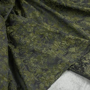 May include: Green fabric with a raised floral pattern. The fabric is textured and has a subtle sheen.