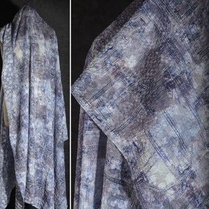 May include: A draped textile with a textured, quilted appearance. The fabric features a pattern of squares and rectangles in shades of blue, gray, and off-white. The overall effect is reminiscent of denim or a patchwork design. The textile is displayed on a mannequin.