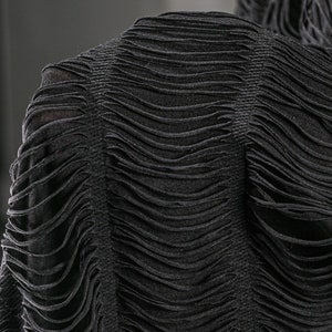 Puede incluir: Tejido de punto negro texturizado con un aspecto desgastado y deshilachado. El tejido est&aacute; recogido y arrugado, creando un dise&ntilde;o &uacute;nico y elegante.