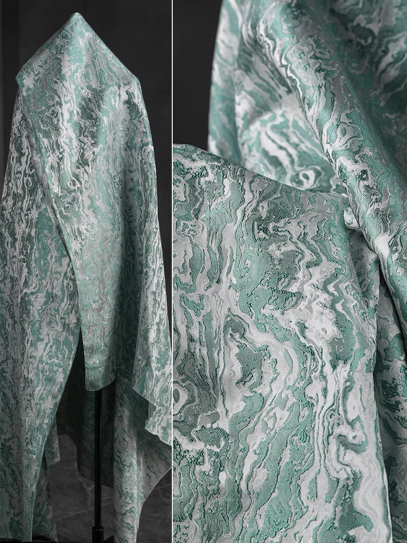 K&ouml;nnte beinhalten: Nahaufnahme eines teal- und wei&szlig;en Stoffes mit Marmormuster. Der Stoff ist &uuml;ber einem St&auml;nder drapiert und hat eine weiche, flie&szlig;ende Textur.