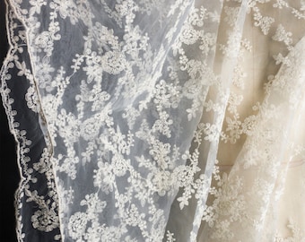 May include: White sheer fabric with a delicate floral lace pattern. The lace is embroidered with small white beads.