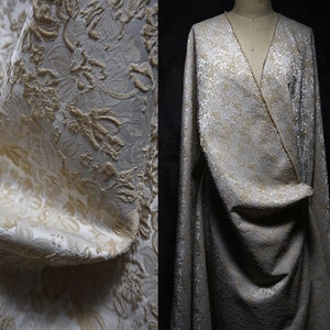 Puede incluir: Primer plano de una tela blanca con un patrón floral en relieve de color beige. La tela está drapeada sobre un maniquí.