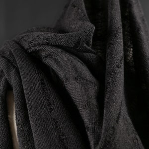 以下が含まれることがあります： 黒色のドレープされた生地のクローズアップ。織り目が粗く、質感があります。生地は折りたたまれ、重ねられており、影と奥行きを作り出しています。素材は軽く、スカーフまたはショールである可能性があります。