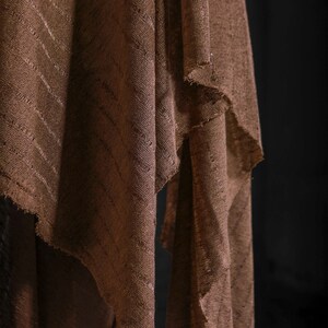 May include: A brown fabric with a striped pattern, folded and draped over a surface. The fabric has a rough, textured surface.