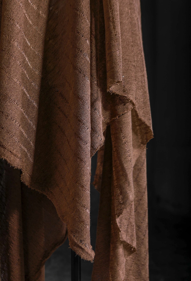 May include: A brown fabric with a striped pattern, folded and draped over a surface. The fabric has a rough, textured surface.