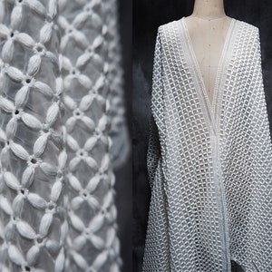 以下が含まれることがあります： 繊細な花柄の白いクロシェ生地。生地は透き通っていて軽量なので、夏の衣服に最適です。