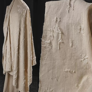 May include: A close-up of a beige fabric with a distressed, textured surface. The fabric has a woven pattern and is slightly frayed at the edges.