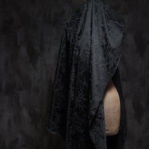 May include: A black fabric with a textured pattern draped over a dress form. The fabric has a subtle sheen and a delicate, almost floral, design.