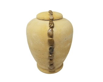 Op de afbeelding: Een beige keramische urn met een decoratieve lijn van bruine stenen rond het midden.