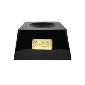 May include: A black, glossy memorial urn with a square base and a recessed top. A gold-colored plaque on the front features an engraved football player and the inscription: "William J. Barrett, April 30, 1942 - June 01, 2004, Always in my Heart."