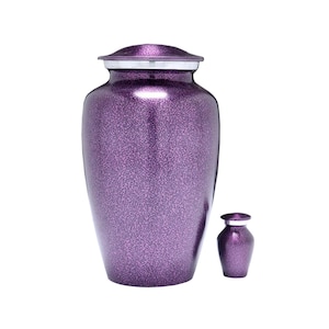 Puede incluir: Un conjunto de dos urnas de cremación de color púrpura. La urna más grande tiene un acabado moteado y una tapa plateada. La urna más pequeña es de color púrpura liso con una tapa plateada.