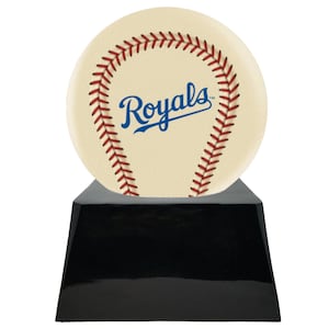 Może przedstawiać: Trofeum o tematyce baseballowej z kremową piłką z czerwonymi szwami i napisem "Royals" w kolorze niebieskim. Piłka spoczywa na błyszczącej czarnej podstawie w kształcie trapezu. Nagroda sportowa.
