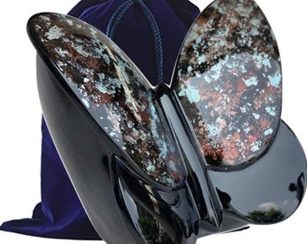 May include: Black butterfly-shaped cremation urn with a blue velvet bag. The urn has a speckled, metallic finish.