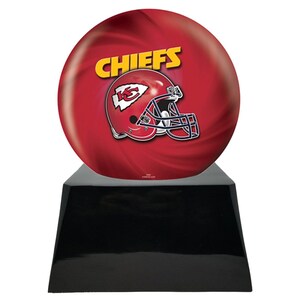 May include: A red and yellow Chiefs football helmet and team name are displayed on a red bowling ball. The bowling ball sits atop a black, glossy, trapezoid-shaped base. The background has a swirling pattern.