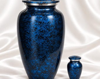 May include: A large and a small cremation urn, both featuring a deep blue and black marbled finish with a glossy surface. Each urn has a cylindrical body, a rounded lid, and a thin silver-toned metal band separating the lid from the base.