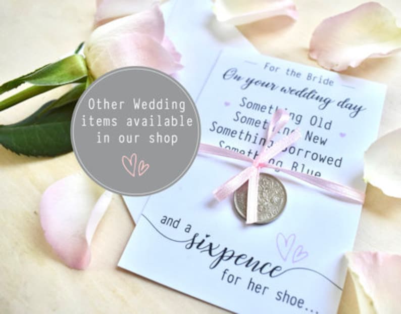 May include: A white card with pink ribbon tied around it. The card has the text "For the Bride On your wedding day Something Old Something New Something Borrowed Something Blue and a sixpence for her shoe..." printed on it. A silver coin is tied to the ribbon.