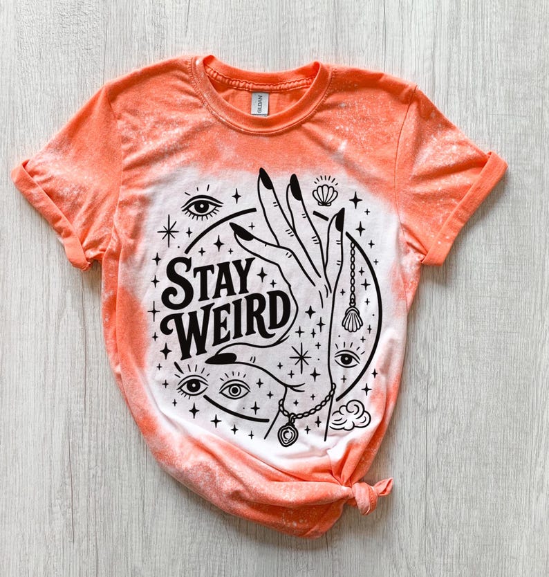 Handmade bleached styles shirt. Close-up of witchy Stay Weird shirt design with celestial artwork, mystical hands, stars, and bold black text