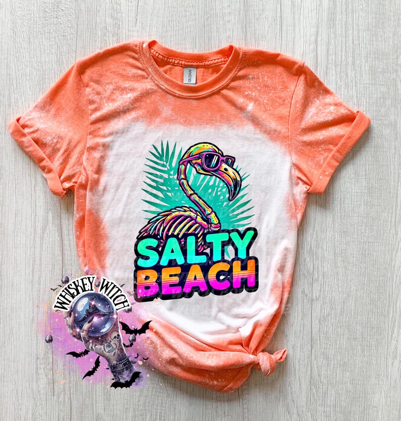 May include: Orange and white t-shirt with a flamingo graphic wearing sunglasses and the words "Salty Beach". The flamingo is in front of green palm leaves. The shirt has a tie-dye effect.