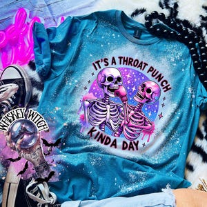 May include: A turquoise blue t-shirt with a bleach-splattered effect. The shirt features a graphic of two skeletons boxing with the text "It's a throat punch kinda day".