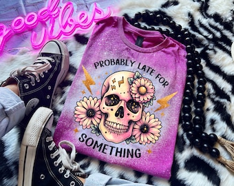 May include: A purple t-shirt with a bleached effect featuring a skull with flowers and the text "Probably Late For Something" in gold glitter.