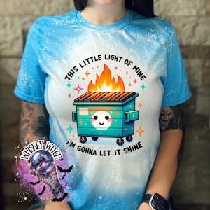 Sapphire Blue  t-shirt with a bleach-splattered design featuring a cartoon dumpster on fire with the text "This little light of mine I'm gonna let it shine".