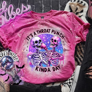 May include: Pink t-shirt with a bleached effect featuring two skeletons wearing boxing gloves and the text "It's a throat punch kinda day".