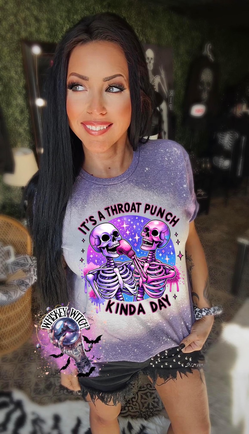 May include: Purple t-shirt with a graphic of two skeletons fist bumping. The skeletons are wearing boxing gloves and the text reads "It's a throat punch kinda day".